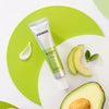 COSNORI Avocado Eye Cream lying on white and green background wit Avocados