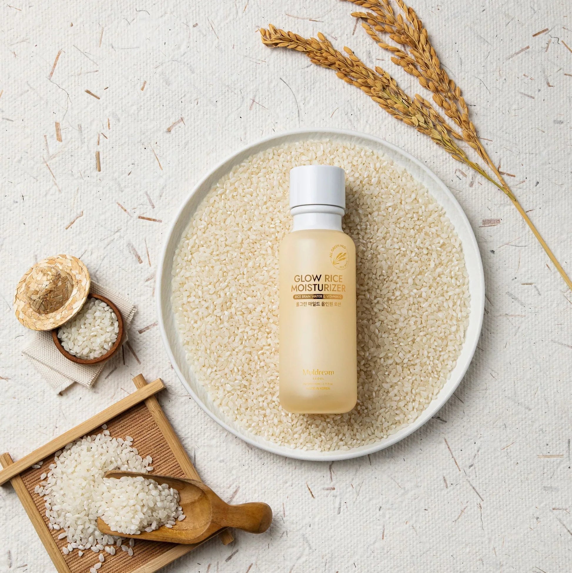 Glow Rice Moisturizer with rice bran water & vitamin C, surrounded by raw rice grains and stalks for natural K-beauty skincare