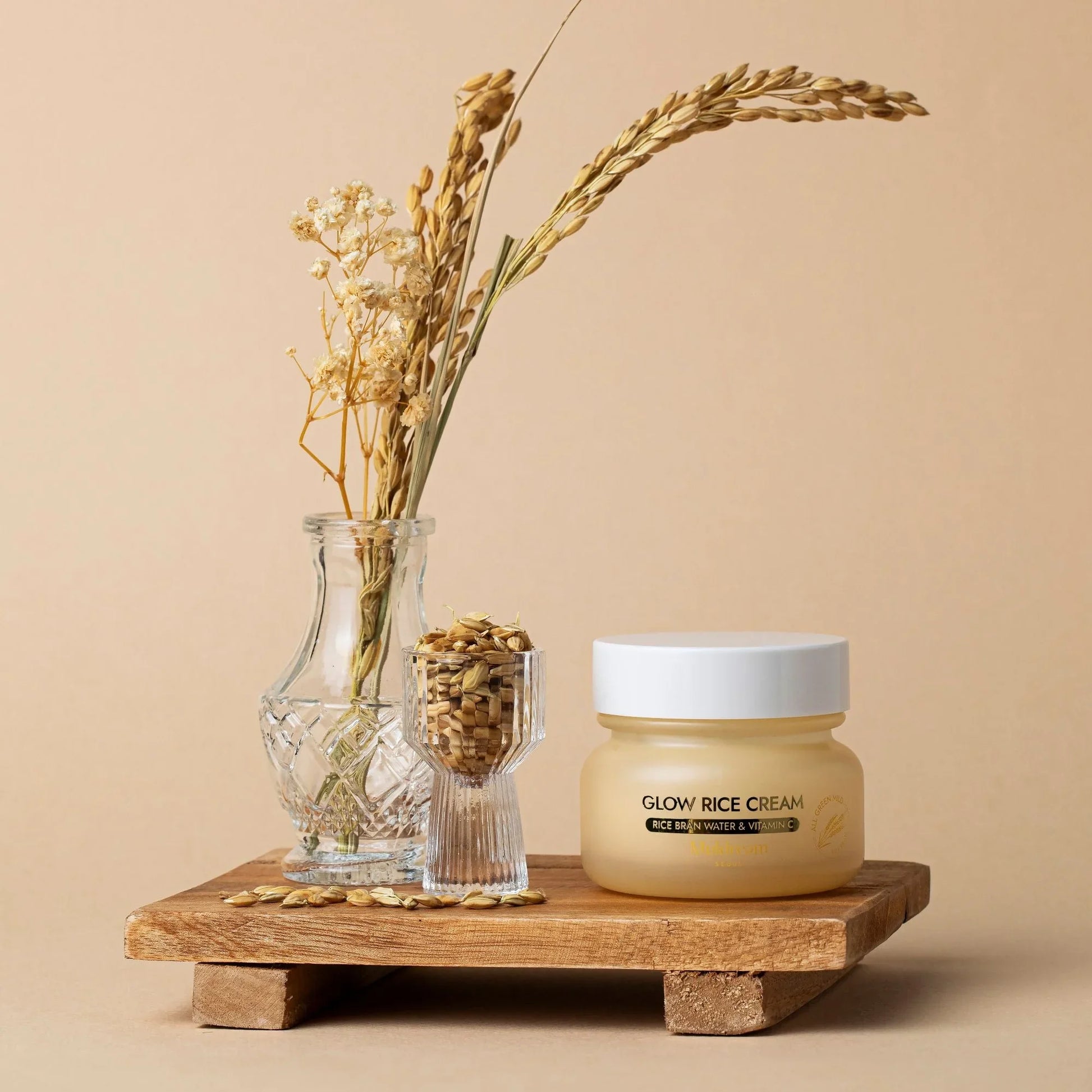 Glow Rice Cream with rice bran water and vitamin C, displayed with dried flowers and rice grains on a wooden tray.