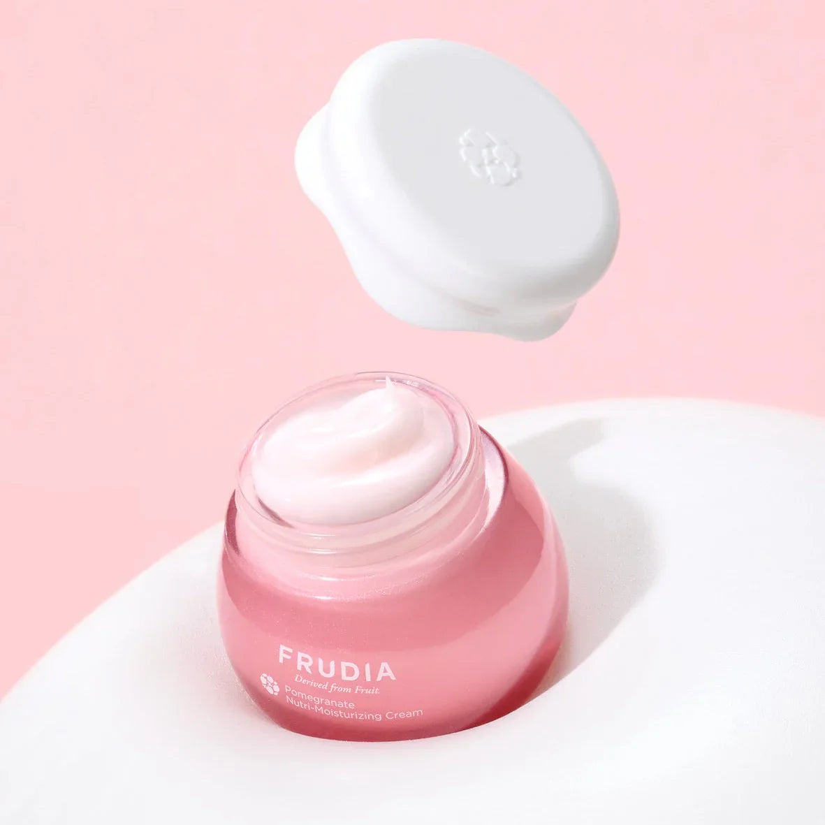 Frudia Pomegranate Nutri-Moisturizing Cream in a pink jar, vegan firming skincare product on white and pink background