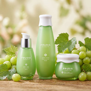 Frudia Green Grape Pore Control skincare set with serum, toner, and cream, surrounded by fresh grapes and leaves.